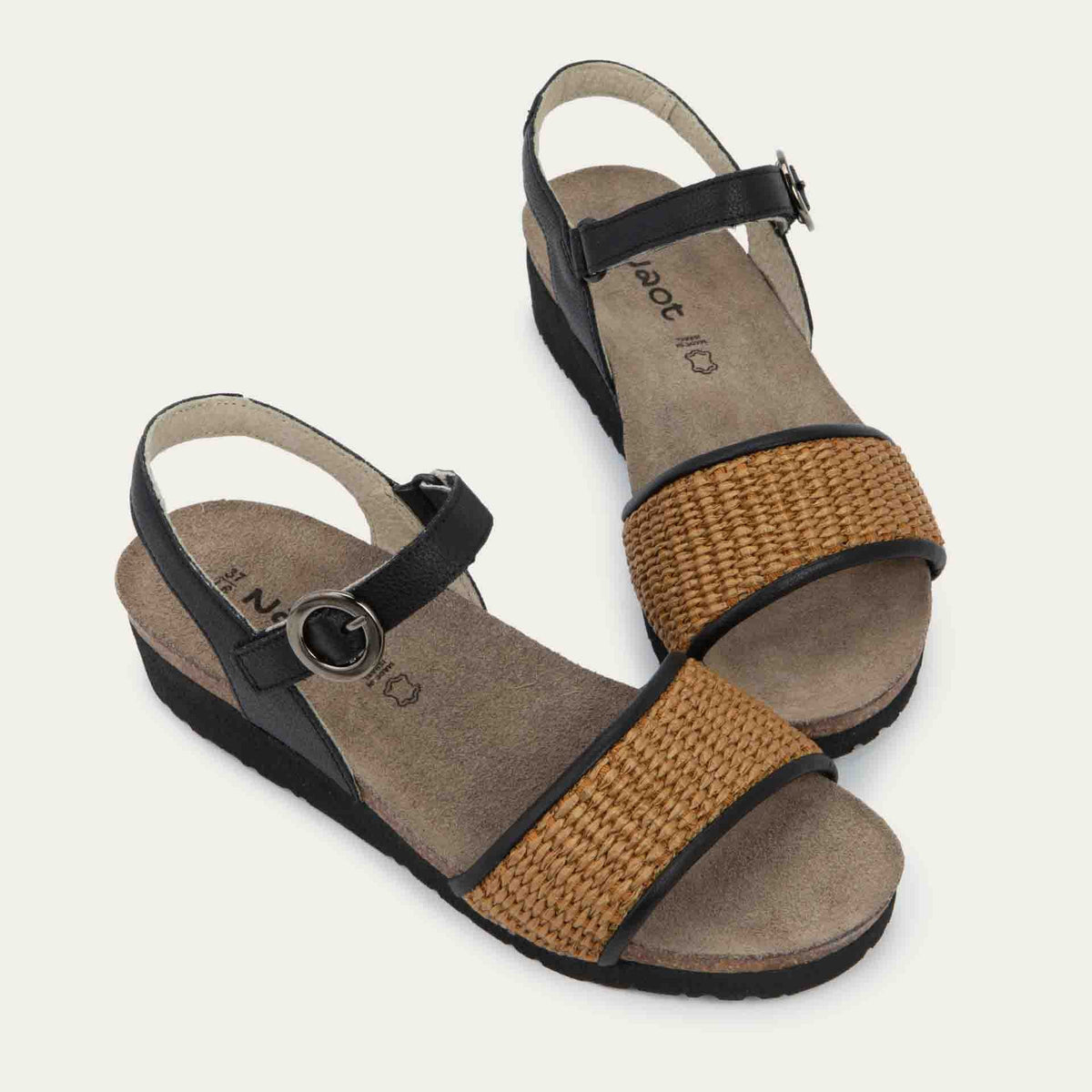 Pair of sandals with a black ankle strap and buckle, cork wedge sole, and a woven tan strap on the front.