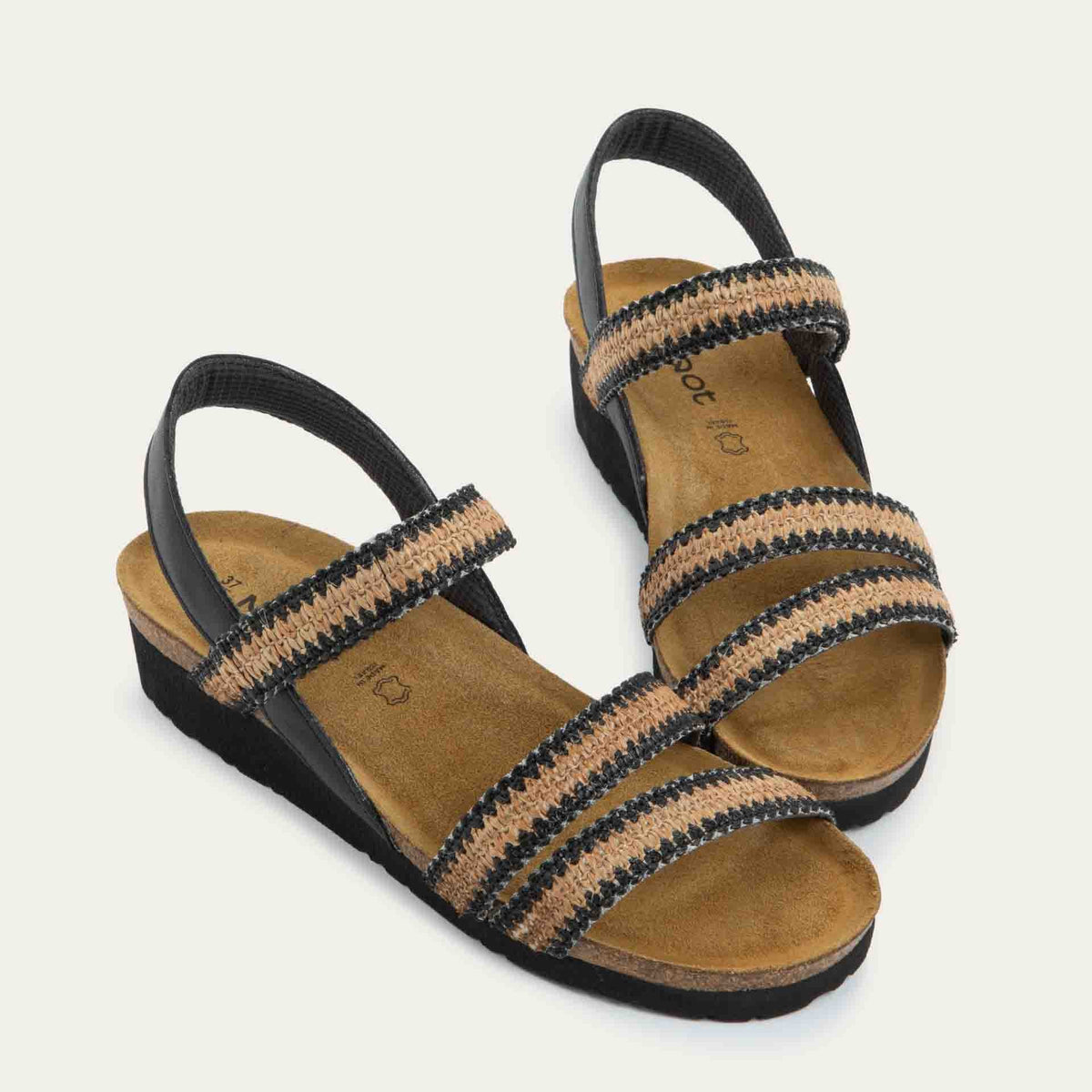 View of a pair of black and brown raffia sandals with a cork footbed, black sole, and triple-strap design including a crisscross ankle strap.