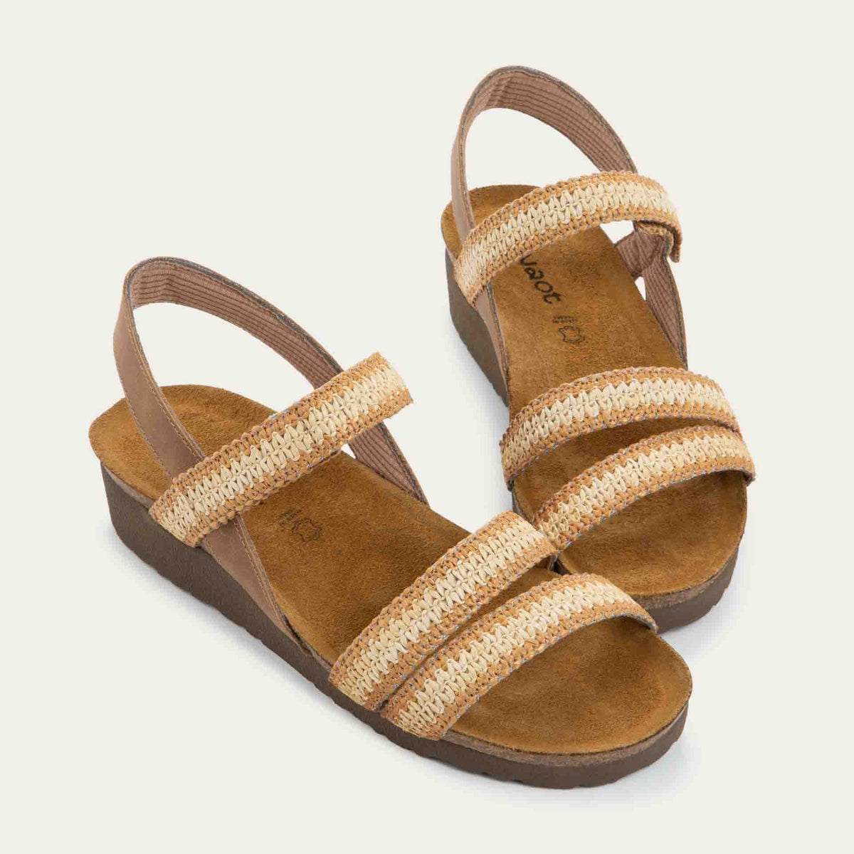 View of a pair of brown and ivory raffia sandals with a cork footbed, black sole, and triple-strap design including a crisscross ankle strap.