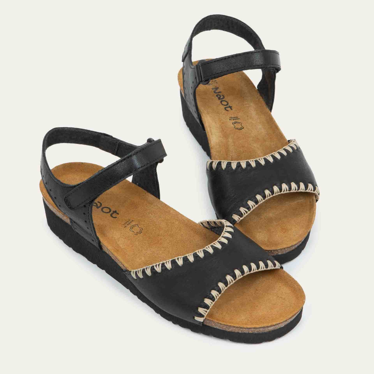View of a pair of black and brown raffia sandals with a cork footbed, black sole, and triple-strap design including a crisscross ankle strap.