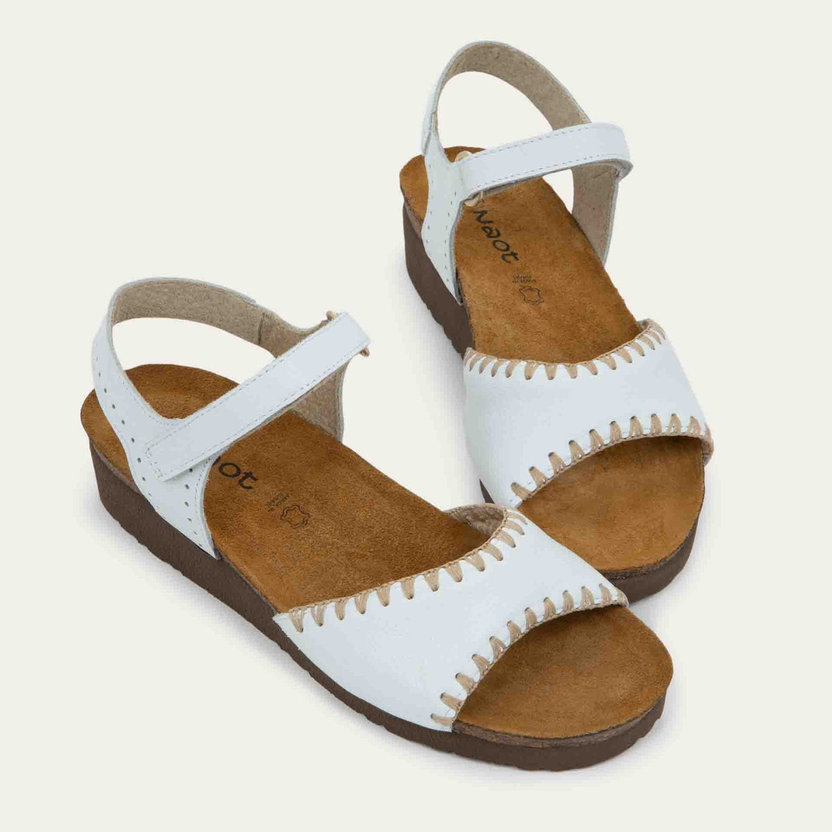 Pair of white sandals featuring a toe strap with contrast stitiching, adjustable ankle strap, and a cork footbed.