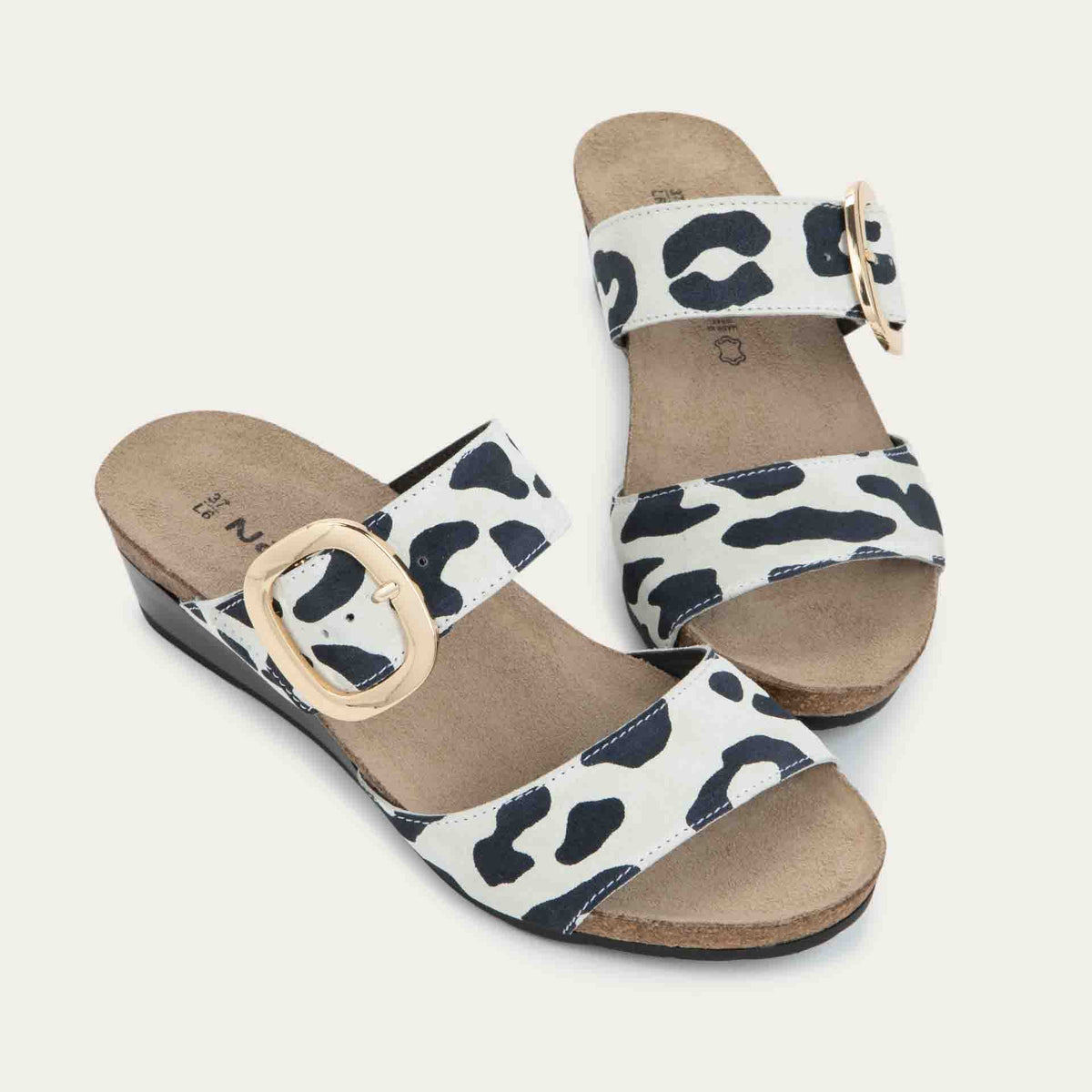 Pair of black and white leaopard-print slip on wedge sandals with two straps and a large gold buckle.