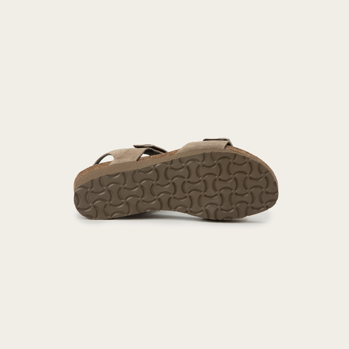 Bottom view of a beige sandal, showing the patterned brown tread of the sole.