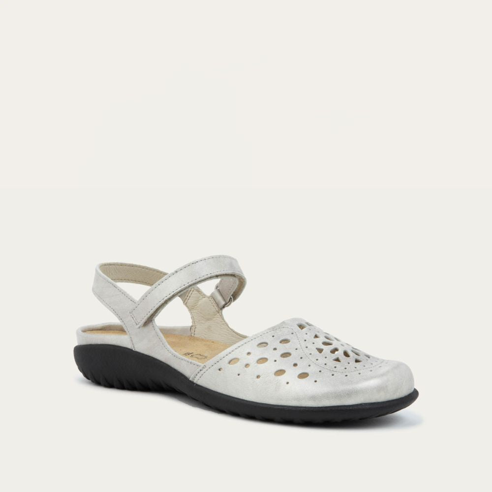 Angled profile view of a silver flat shoe with a perforated design, open heel, and adjustable ankle strap on a black sole