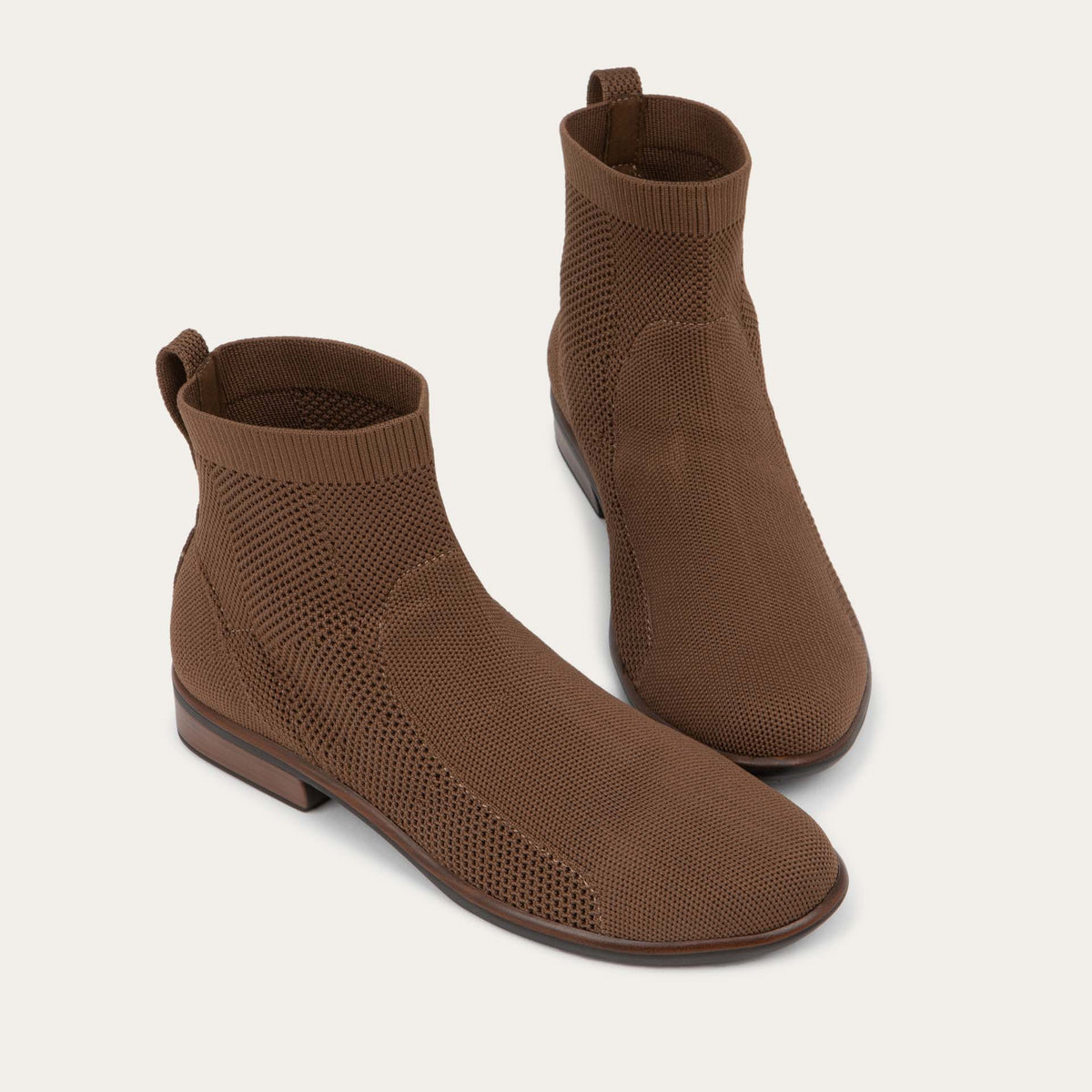 A pair of of brown ankle boots featuring a textured knit uppers, pull tabs at the heels, and low, flat brown soles.