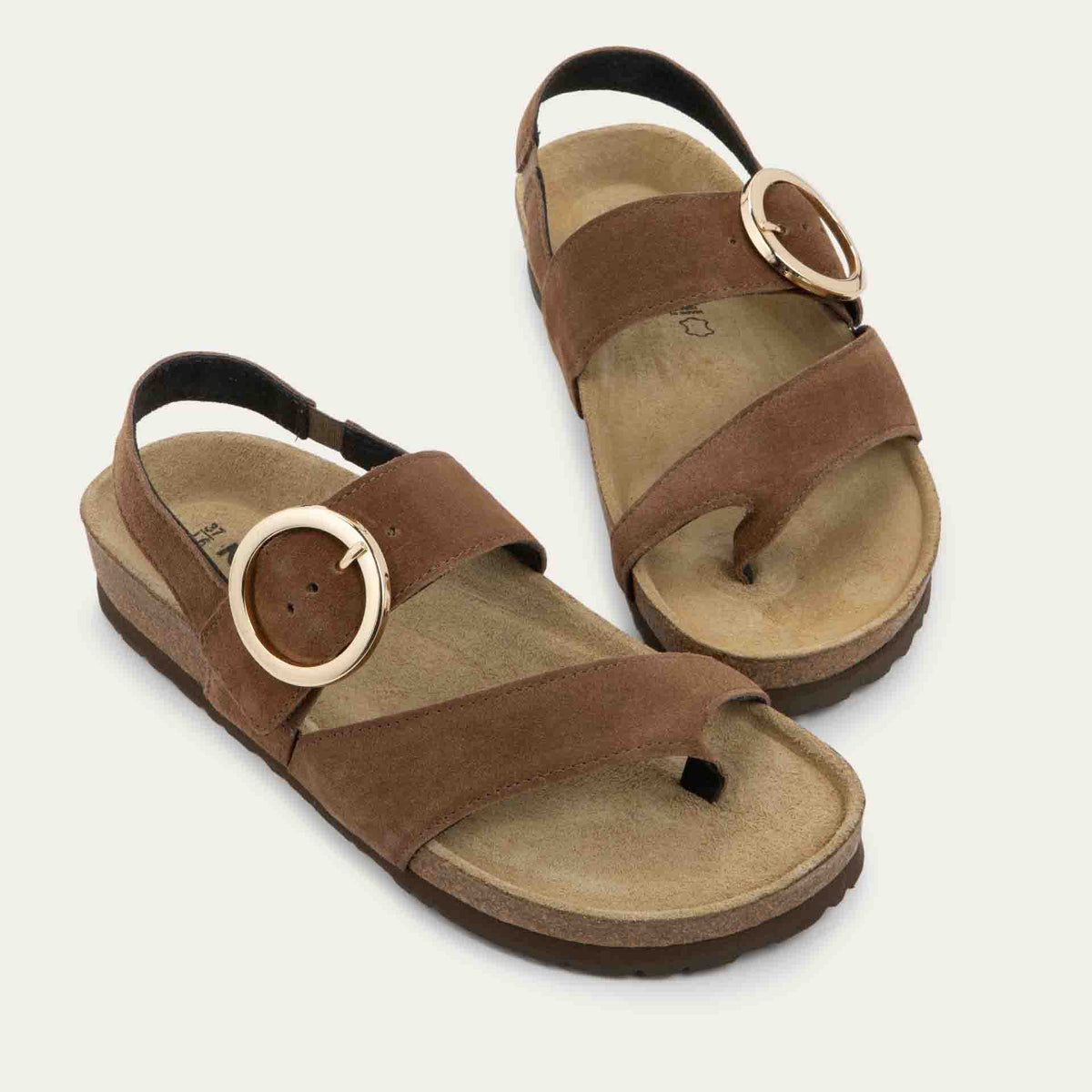Pair of brown strappy slides with an oversized buckle and a toe thong, featuring a cork sole.