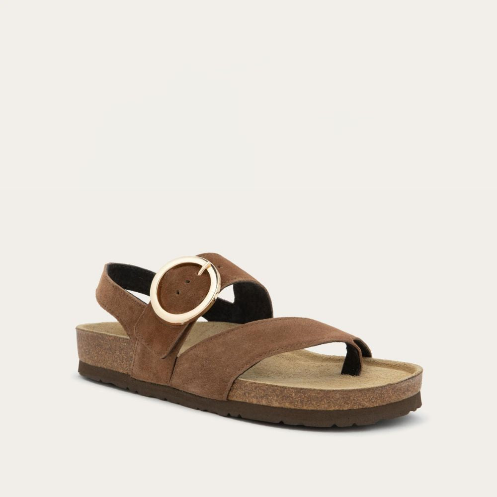Angled profile view of a brown strappy slide with an oversized buckle and a toe thong, featuring a cork sole.