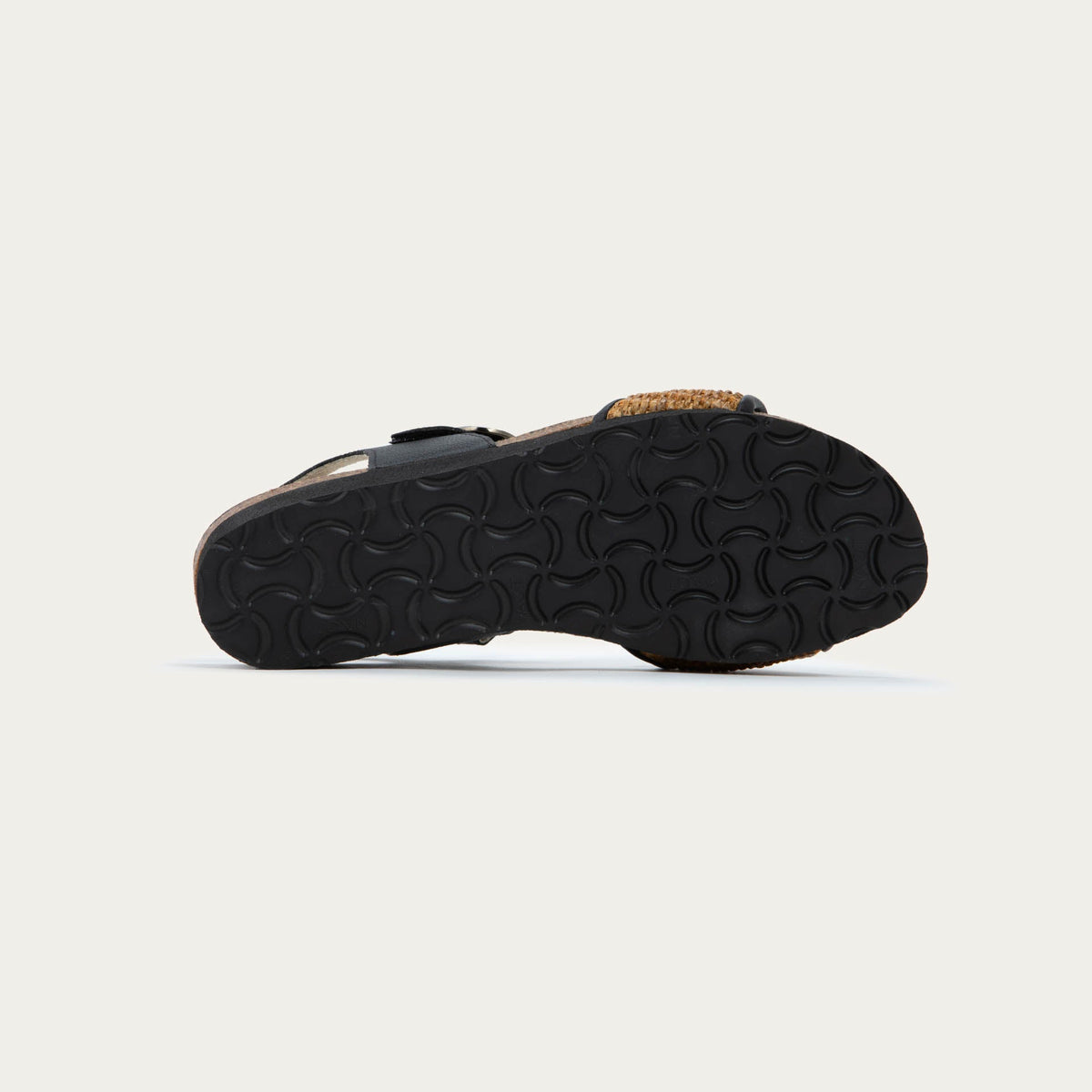 Bottom view of a sandal with a black ankle strap and buckle, cork wedge sole, and a woven tan strap on the front. 