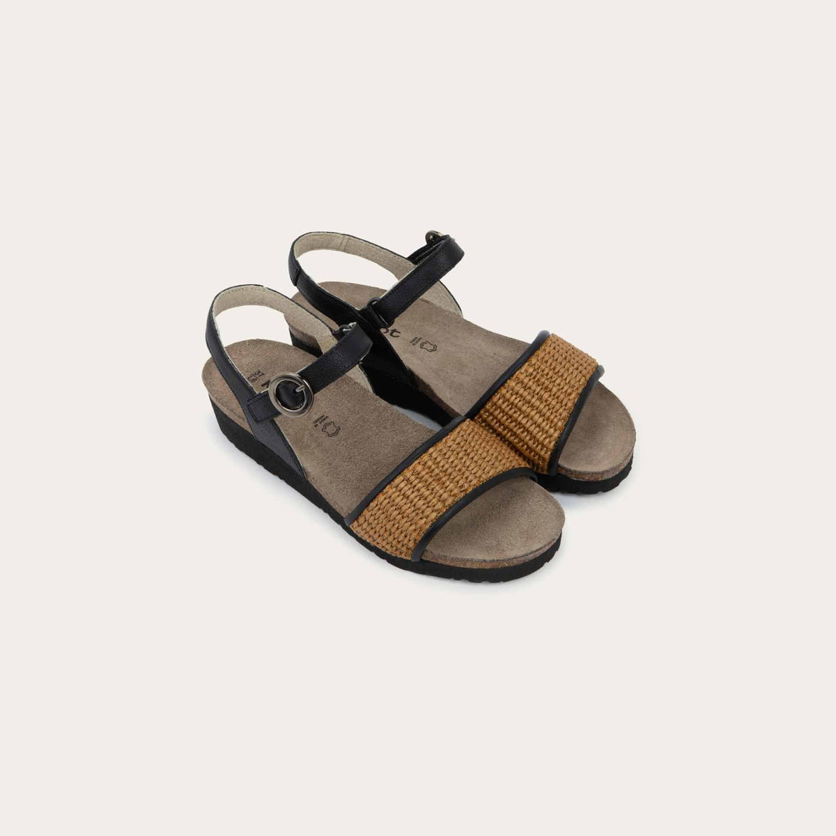 Pair of sandals with a black ankle strap and buckle, cork wedge sole, and a woven tan strap on the front. 
