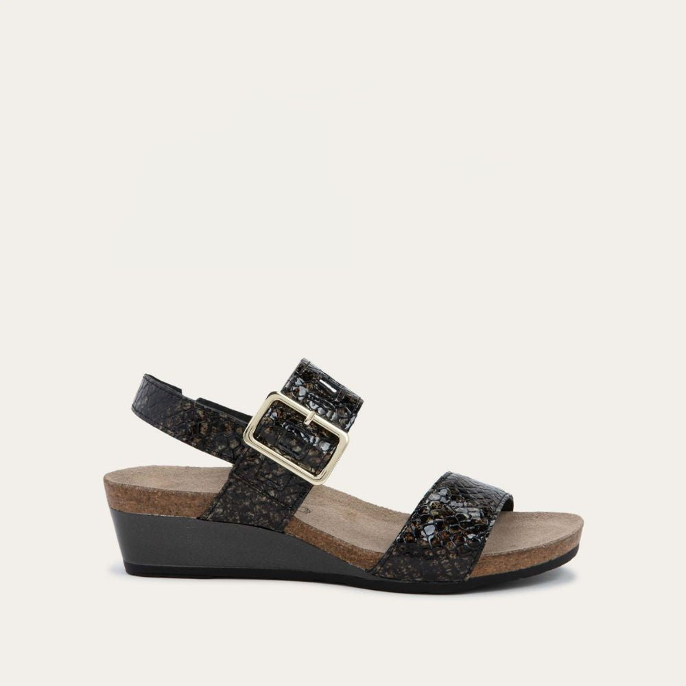 Profile view of a black wedge sandal with a snakeskin design, featuring two straps and a metallic buckle with a cork footbed.