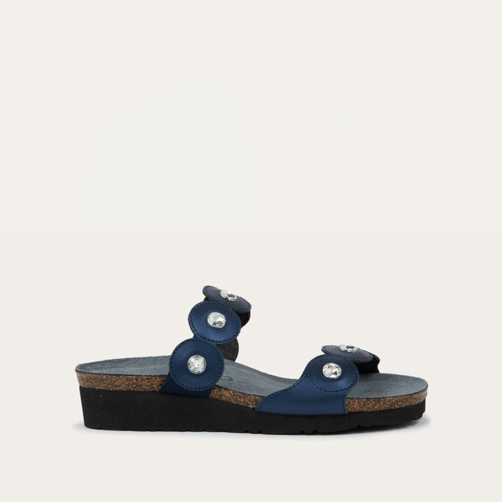 Profile view of navy blue sandal with cork wedge sole. Features two straps with circular details and large round silver studs.