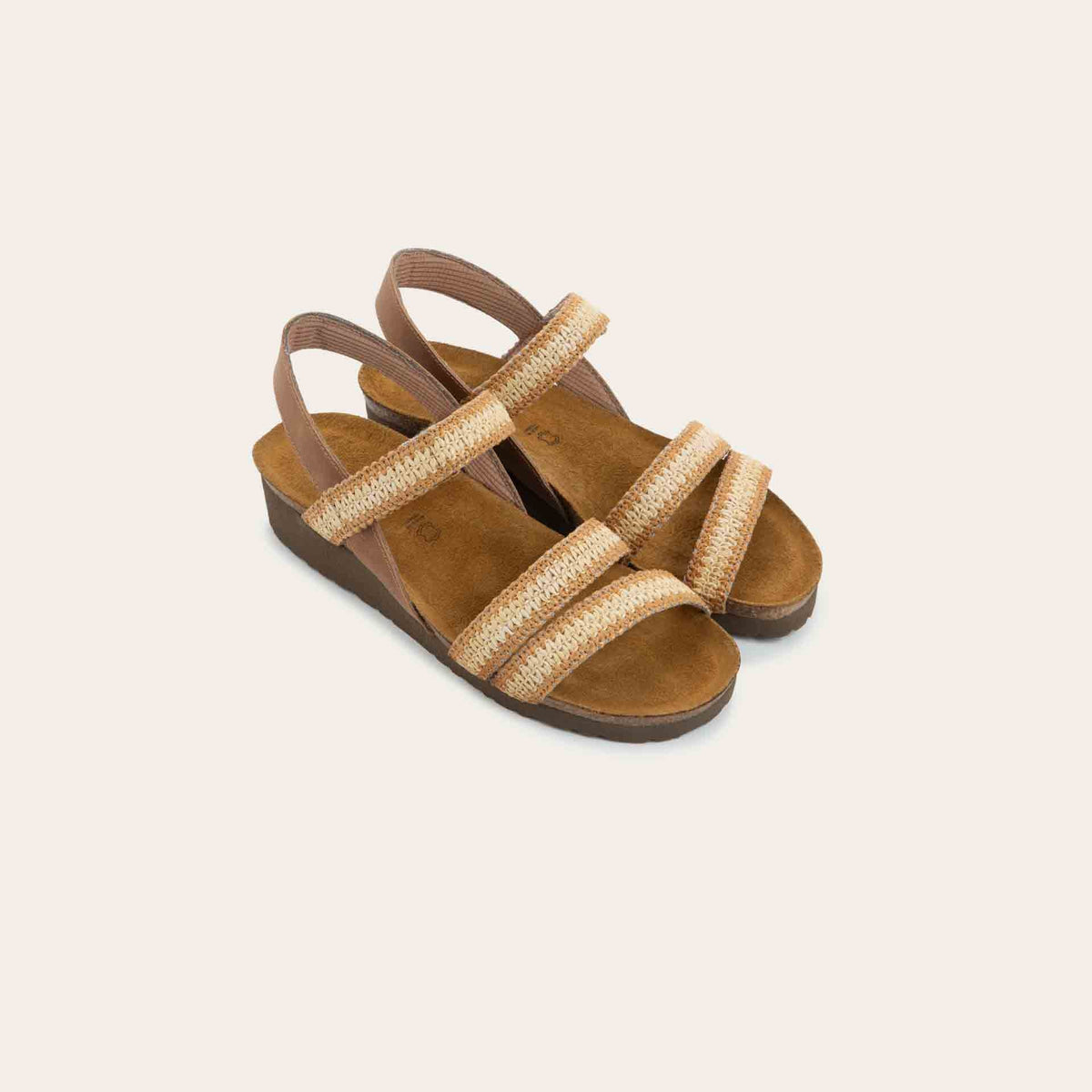 View of a pair of  brown and ivory raffia sandals with a cork footbed, black sole, and triple-strap design including a crisscross ankle strap.