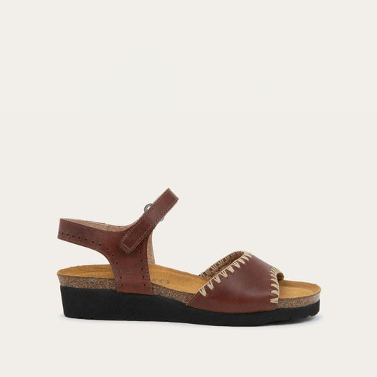 Profile view of  a brown sandal featuring a toe strap with contrast stitiching, adjustable ankle strap, and a cork footbed.