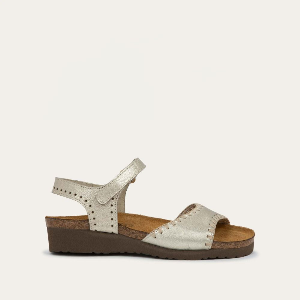 Profile view of  a gold sandal featuring a toe strap with contrast stitiching, adjustable ankle strap, and a cork footbed.