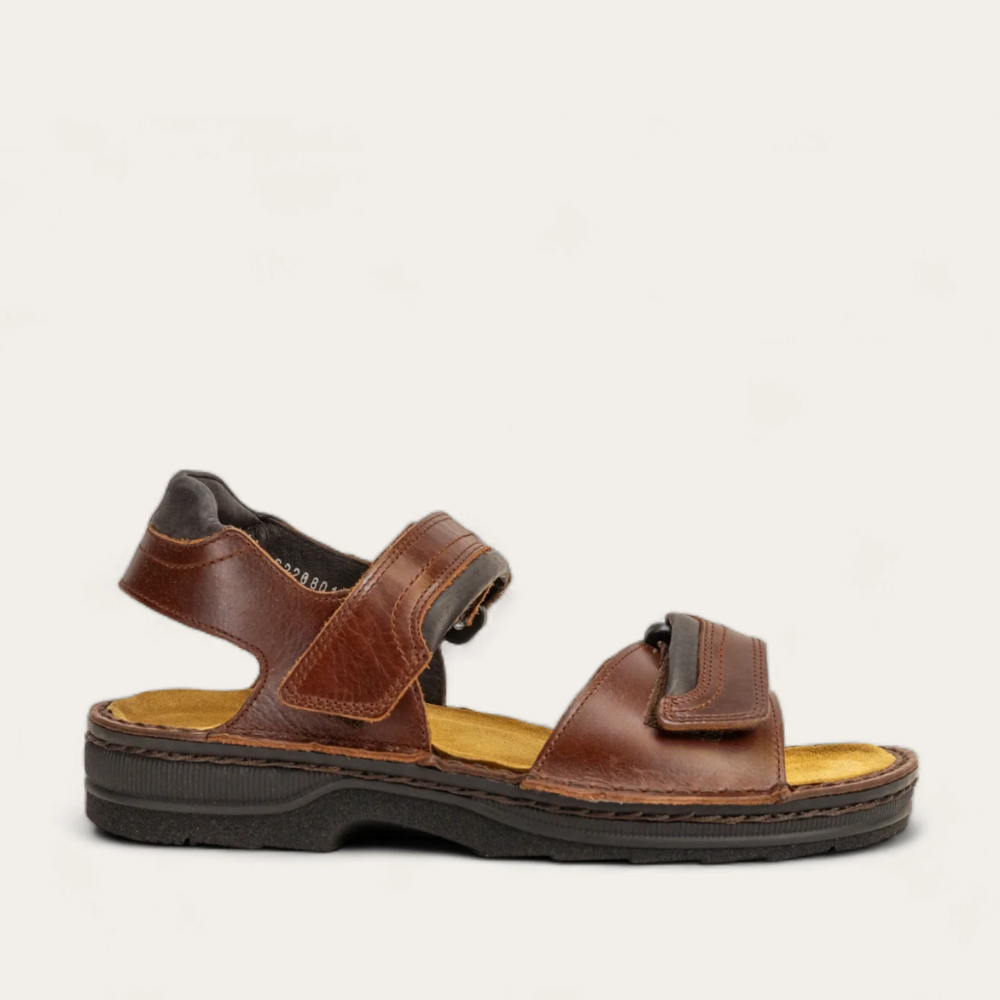 A brown, adjustable backstrap sandal with two hook and loop straps at the instep, featuring a cork and latex footbed wrapped in suede and a polyurethane sole.