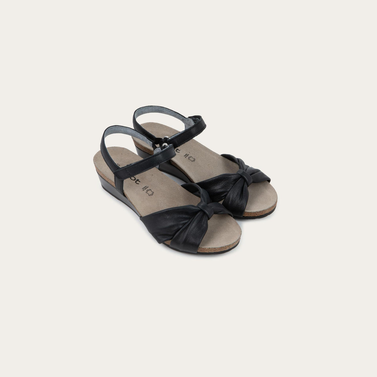 A pair of  black wedge sandals with an ankle strap and twisted front strap, featuring a cork footbed and wedge heel. 