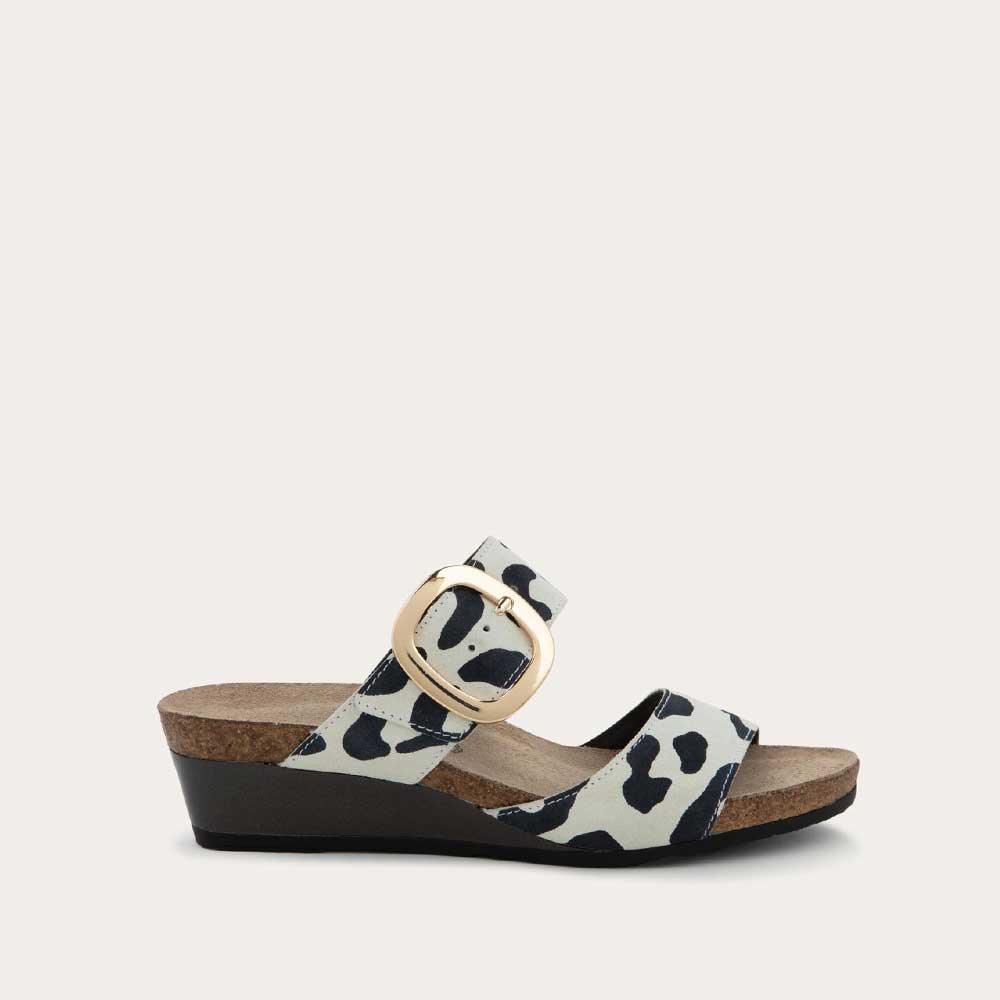 Profile view of a black and white leaopard-print slip on wedge sandal with two straps and a large gold buckle. 