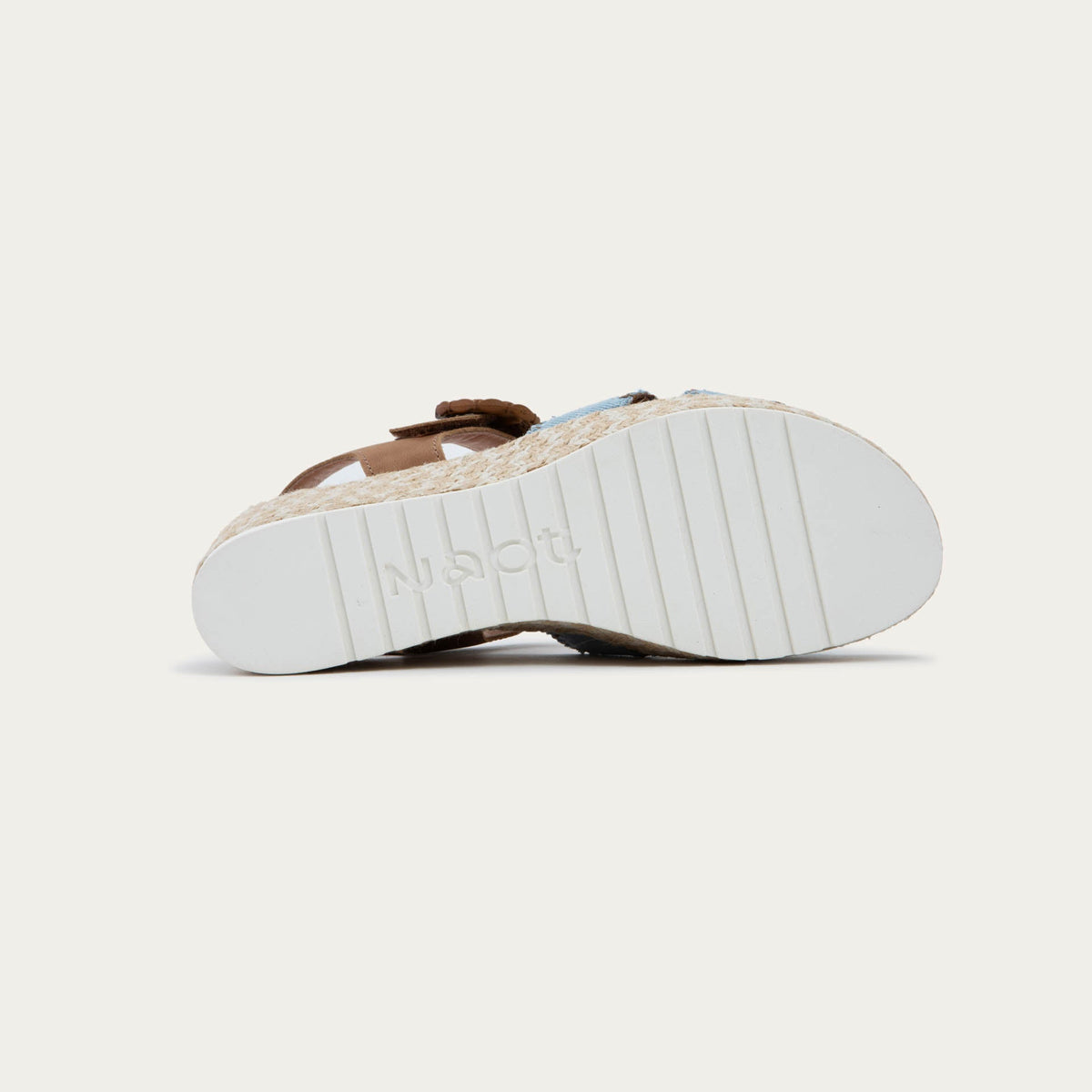Bottom view of a blue/brown wedge sandal with a woven platform and brown leather ankle strap, fastened by a circular buckle. 
