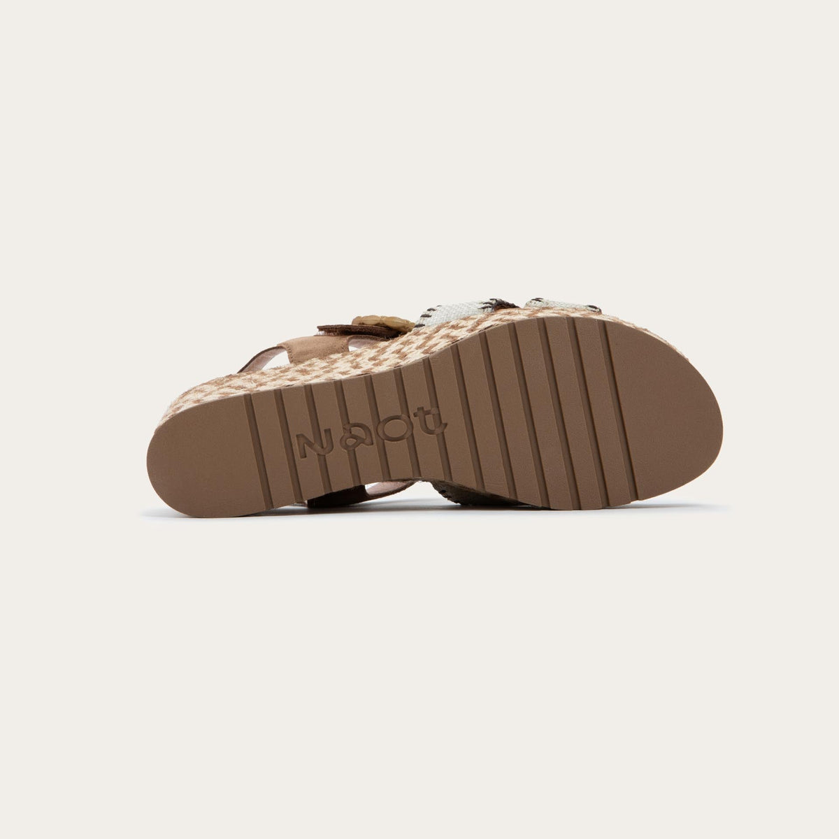 Bottom view of a beige/brown wedge sandal with a woven platform and brown suede ankle strap, fastened by a circular buckle. 