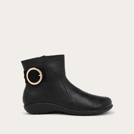 Profile view of a black boot featuring an accent strap with round buckle in the back of the shoe on a dark sole.