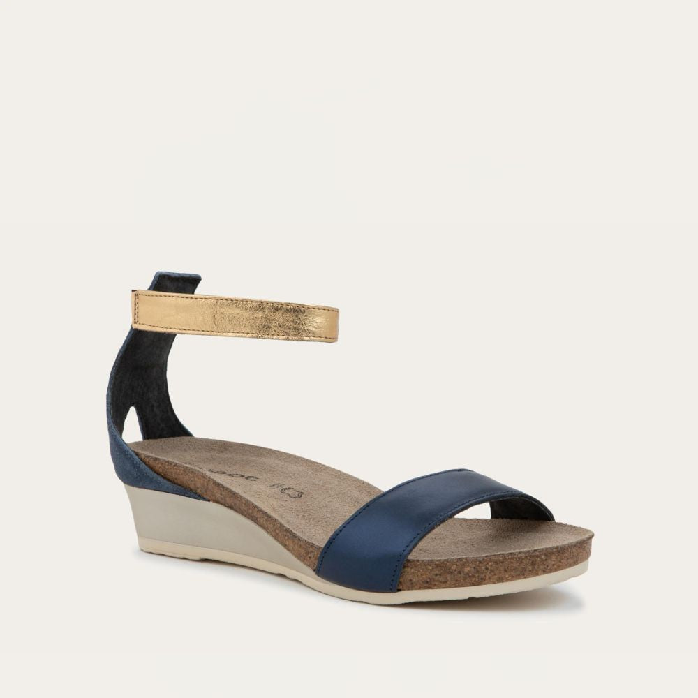 Angled profile view of a blue wedge sandal with cork sole, featuring an open toe and metallic gold ankle strap.