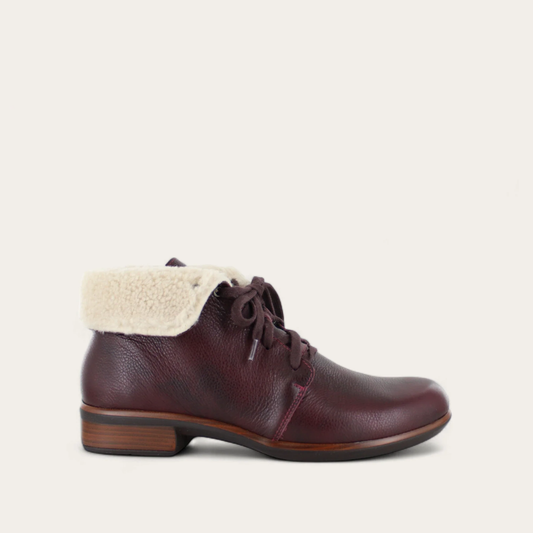 A brown ankle boot with a faux shearling cuff and lace up closure, set on a low heel.
