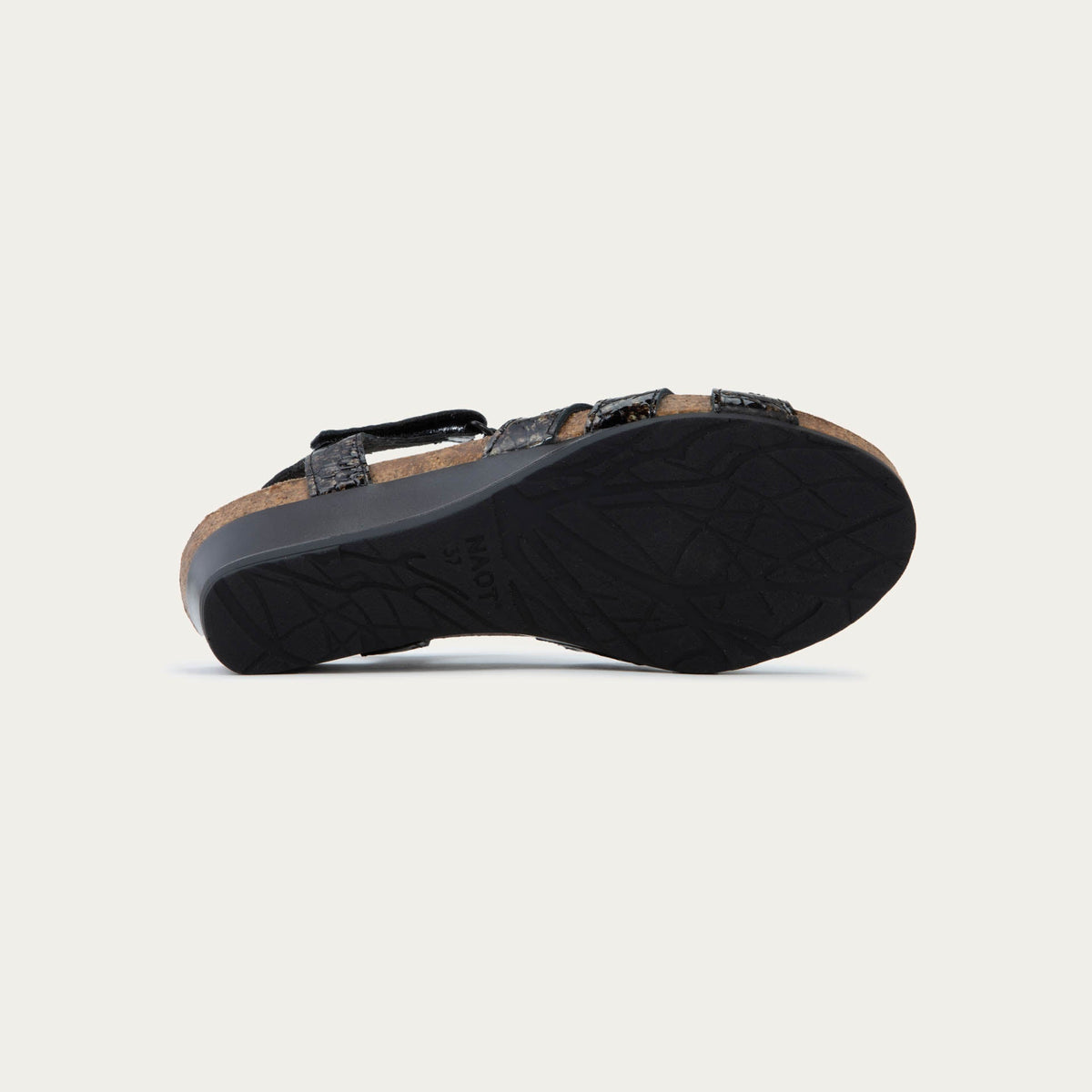 Bottom view of a  reptile printed wedge sandal with strappy design, open toe, and adjustable ankle strap on a cork footbed.