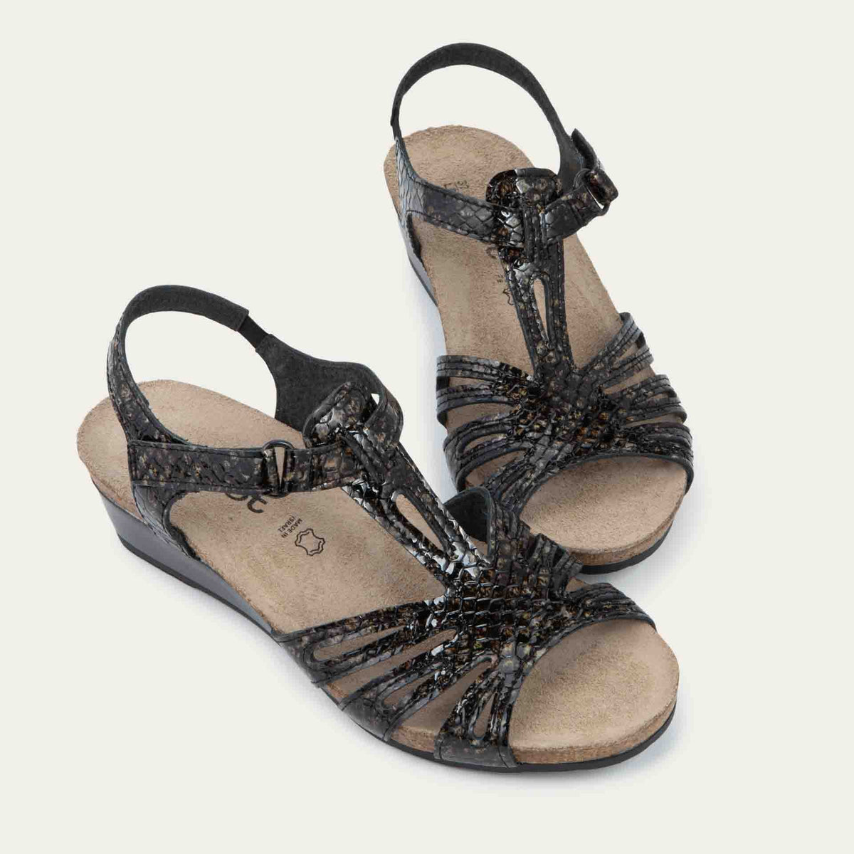 A pair of reptile printed wedge sandals with strappy design, open toe, and adjustable ankle strap on a cork footbed.