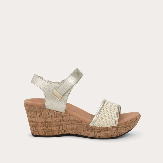 Profile view of a wedge heeled sandal with a gold leather ankle strap, and woven tan front strap