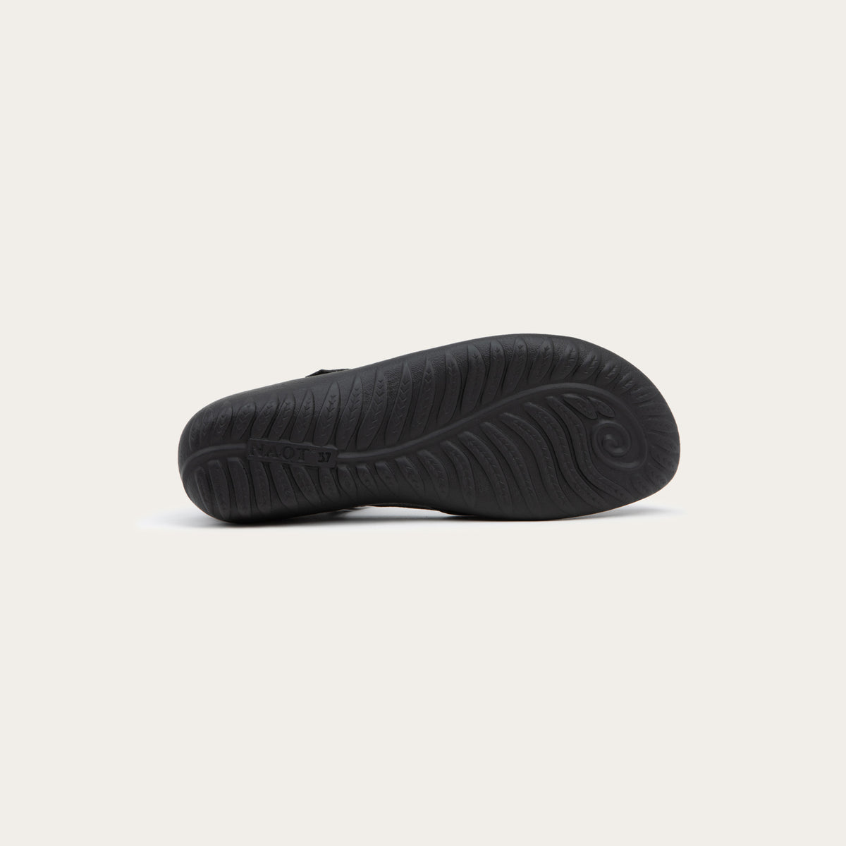 Bottom view of a black Mary Jane featuring contrasting materials and cutouts by the heel on a dark sole.