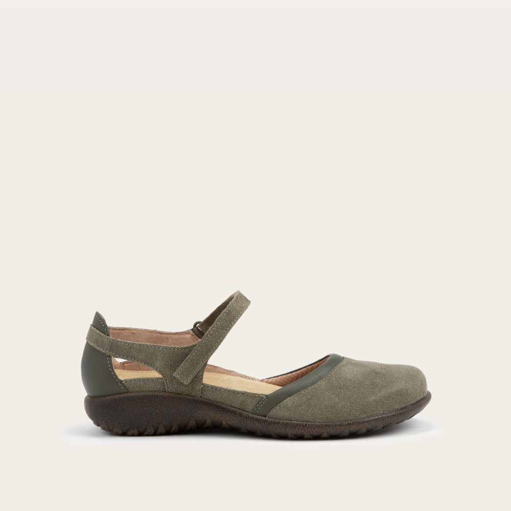 Profile view of a green Mary Jane featuring contrasting materials and cutouts by the heel on a dark sole.