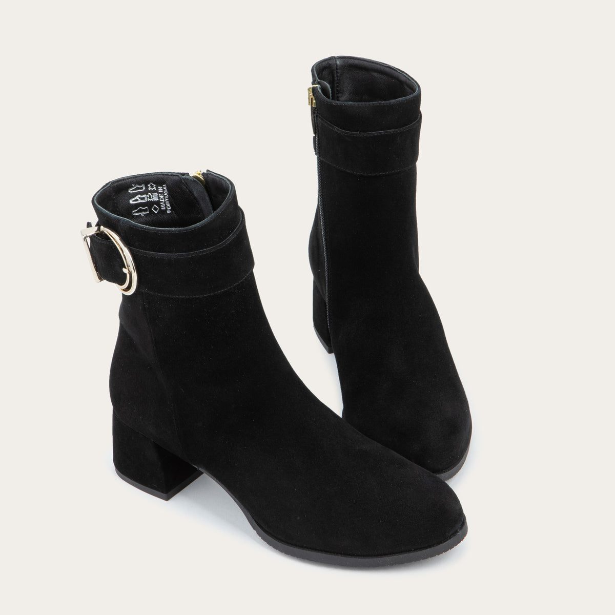 A pair of black suede ankle boots featuring a low block heels and a decorative gold-toned buckle straps around the ankle.