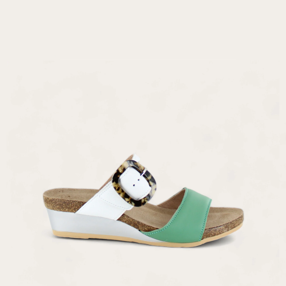 A green and white sandal with an oversized buckle, featuring a cork heel and suede upper.