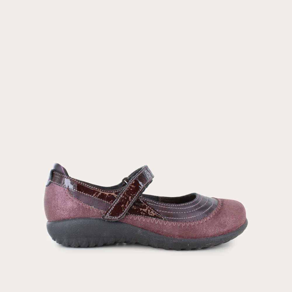 Profile view of a purple mary jane featuring contrasing shimmer suede and shiny leather on a black sole.